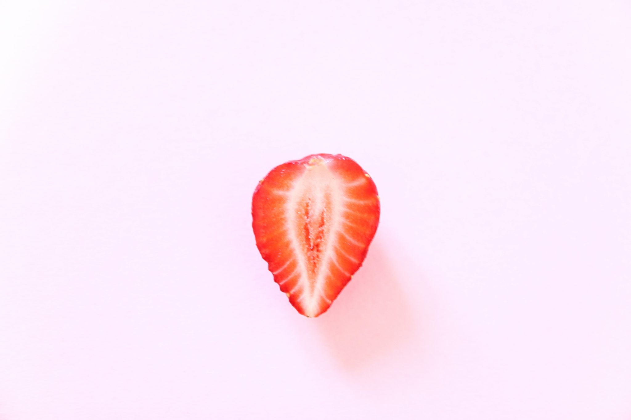 Et jordbær delt i to, med en lyserosa bakgrunn