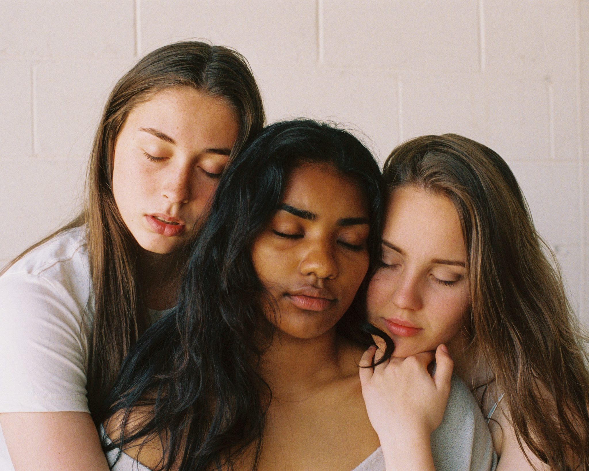 Bilde av tre unge kvinner som klemmer hverandre, med øynene lukket