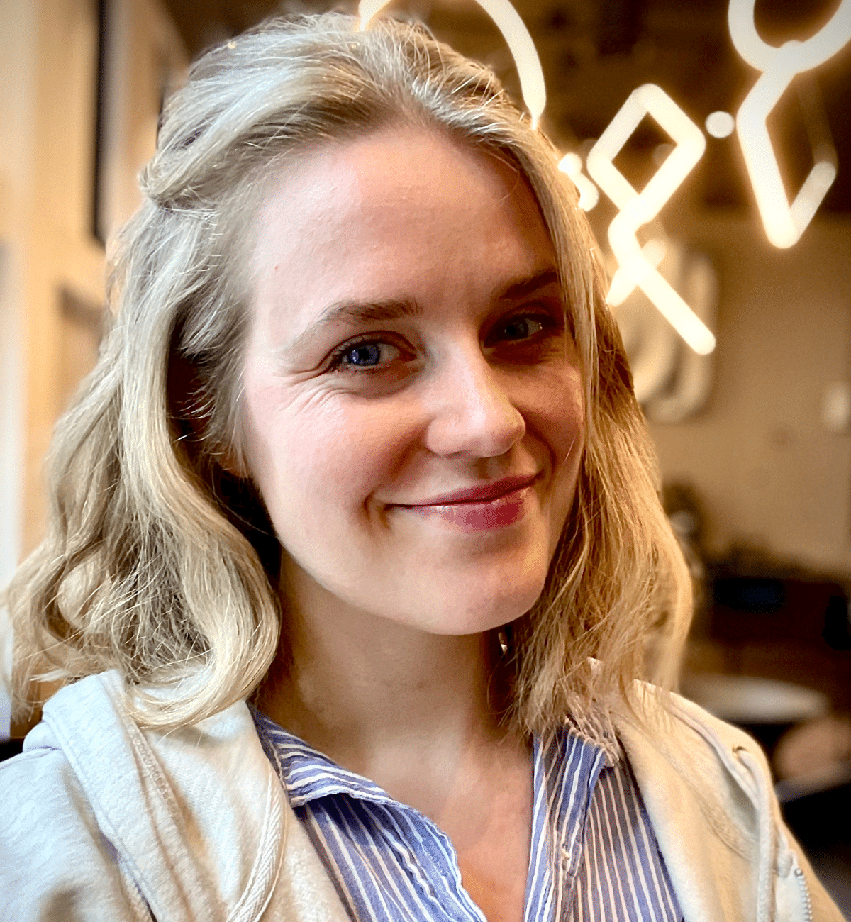 Portrettbilde av Ane Løvereide, en ung kvinne som smiler til kamera. Hun har kort, blondt hår og en lys skjorte.